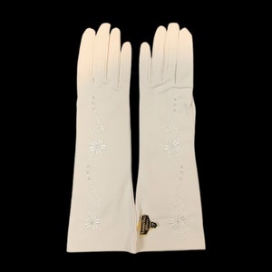 May include: A pair of off-white elbow-length gloves featuring a delicate embroidered floral vine pattern with small clear embellishments. A small black and gold tag attached to the wrist area displays the text Rendez-Vous Gloves and the number 7.