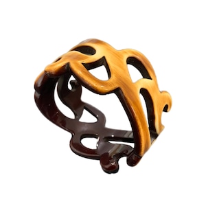 Peut inclure: Une pince à cheveux en plastique marron et beige avec un motif décoratif ajouré.