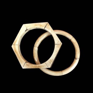 May include: Two off-white bangles with a smooth, polished finish. One bangle features a distinct hexagonal shape with visible segmented joints, while the second bangle is a classic circular hoop. Both items display natural cream-colored tones.