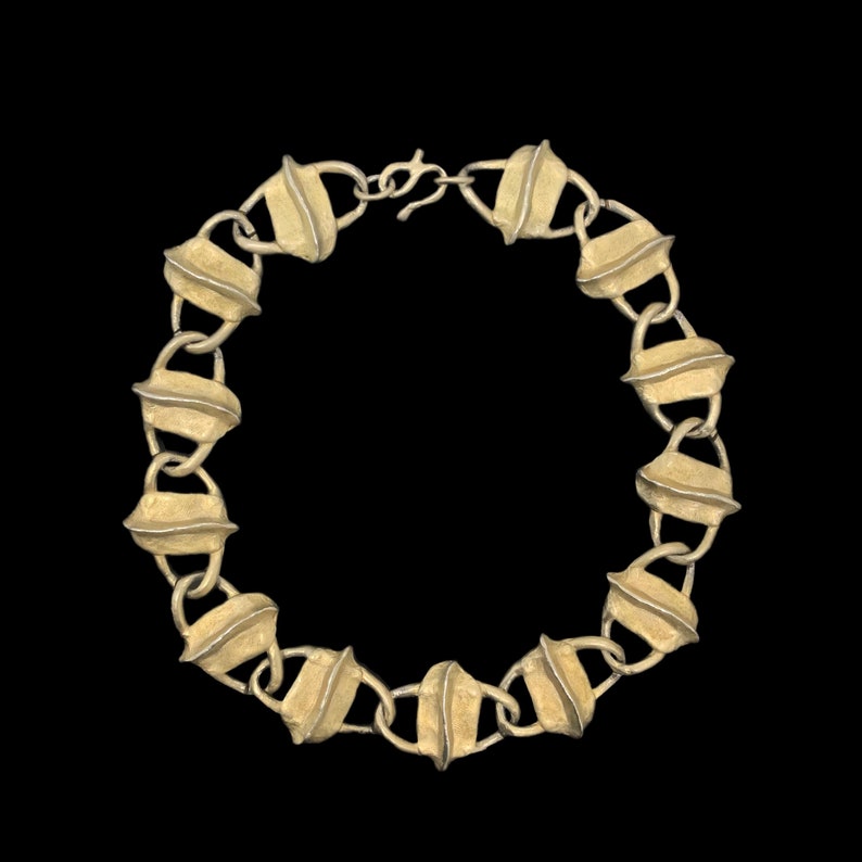 May include: A gold-toned necklace composed of repeating, textured, leaf-shaped links connected by small circular loops. The metal surface features a matte, brushed finish with a central ridge on each link. The necklace includes a lobster claw clasp.