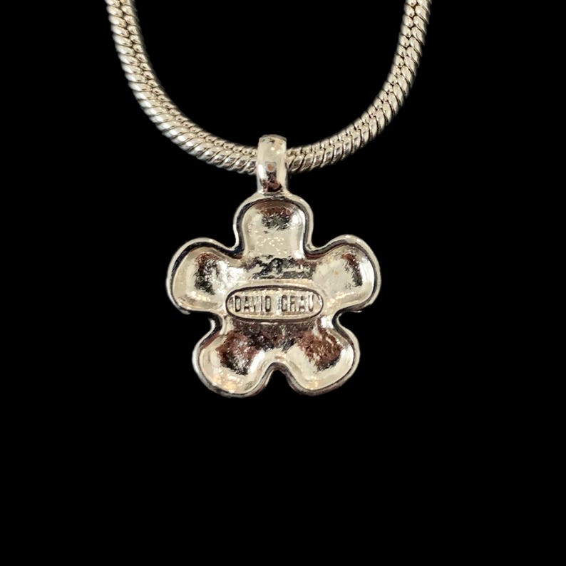 May include: Silver chain necklace with a silver flower pendant. The back of the pendant has the words "David Yurman" engraved on it.