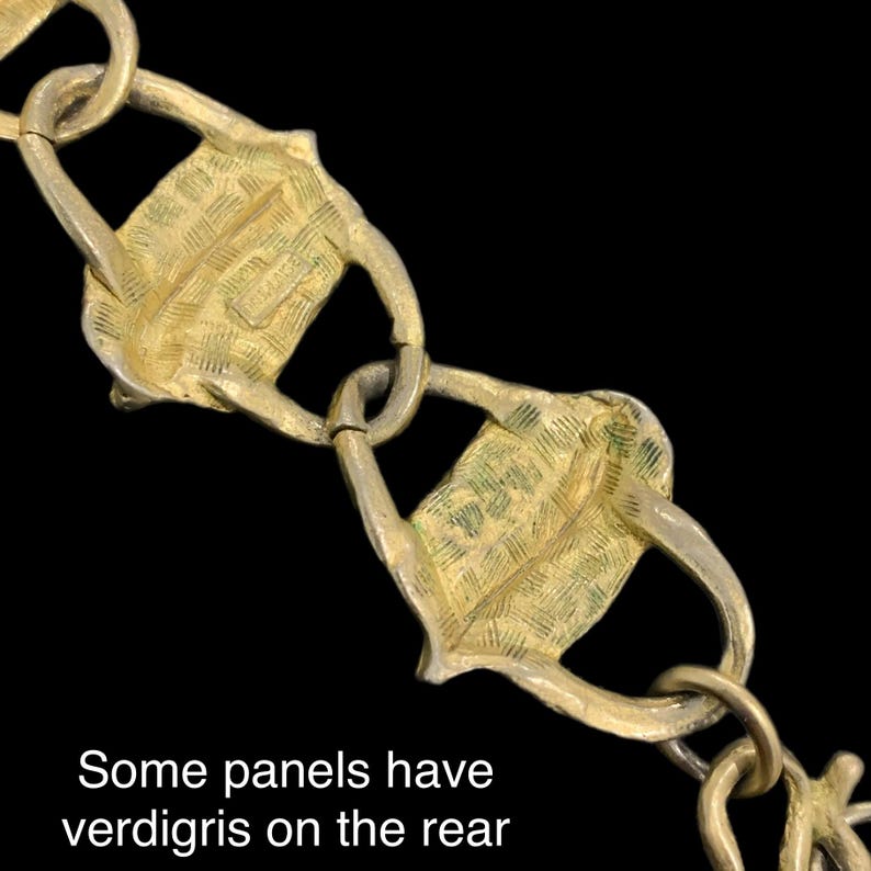 May include: A gold-toned metal chain bracelet composed of rectangular panels with a cross-hatched texture, connected by oval links. The metal shows signs of wear and verdigris. The text "Some panels have verdigris on the rear" is visible.