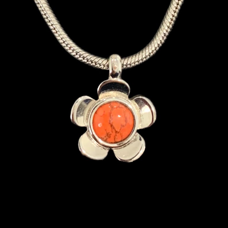 May include: A silver flower pendant necklace with a bright orange stone in the center.