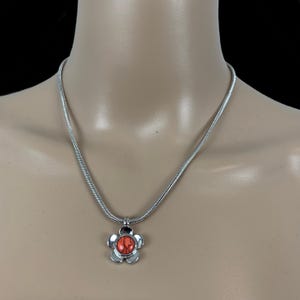 May include: A silver chain necklace with a flower pendant. The flower has a red center stone.