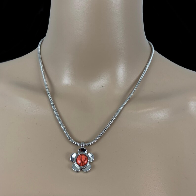 May include: A silver chain necklace with a flower pendant. The flower has a red center stone.
