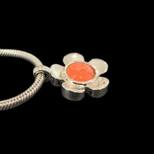 May include: A silver charm necklace with a flower pendant. The flower has a red center stone.