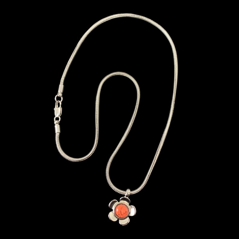May include: A silver chain necklace with a flower pendant. The flower has a coral-colored center.