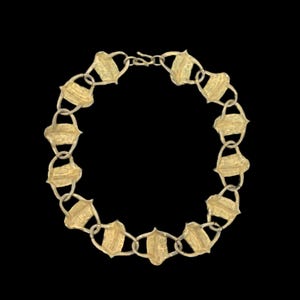 May include: A gold-toned necklace composed of a series of repeating shield-shaped links connected by small circular rings. The metal surface features a textured, matte finish throughout the entire piece, which is secured with a simple hook clasp.