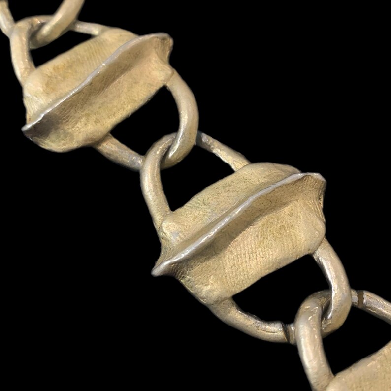 May include: A chain necklace featuring alternating links of textured, matte gold-toned rectangular segments and smooth, silver-toned circular connectors. The gold segments have a raised central ridge and a rough, granular surface texture throughout.