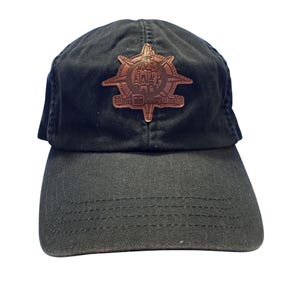 May include: Black baseball cap with a brown leather patch featuring a compass design and the words "Walt Disney World". The cap has a curved peak and a fabric strap closure.