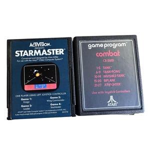 Puede incluir: Dos cartuchos de juegos Atari vintage. Uno está etiquetado como "StarMaster" con un gráfico temático espacial. El otro es "Combat" con una lista de modos de juego. Ambos son negros con texto y gráficos coloridos.