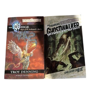 May include: Two paperback books from the Forgotten Realms series. The book on the left is titled "The Siege" by Troy Denning, featuring a winged figure with a spear. The book on the right is "Ghostwalker" by Erik Scott de Bie, with a ghostly figure.