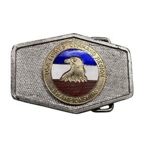 Op de afbeelding: Zilverkleurige metalen gesp met een getextureerd oppervlak. De gesp heeft een cirkelvormig embleem met een Amerikaanse zeearend en de tekst "USA Forces Command Region Championships" in een gouden rand, met rode, witte en blauwe accenten.