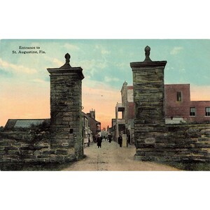 May include: A vintage postcard depicting the entrance to St. Augustine, Florida. The image shows a stone archway with two tall stone pillars, and a street lined with buildings in the background. The sky is a soft pink and orange.