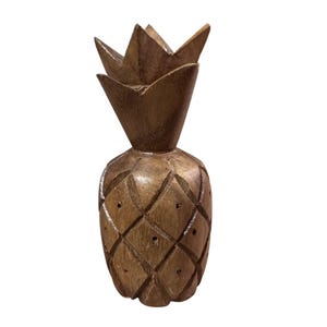 May include: A carved wooden pineapple figurine. The pineapple is a warm brown color with a diamond pattern on the body and a spiky crown. The figurine is a decorative item, likely for home decor.