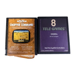 May include: Two vintage video game cartridges. One is labelled "Chopper Command" by Activision, featuring a game screen graphic. The other is a "Tele-Games" cartridge for "Baseball". Both are black with colourful labels.