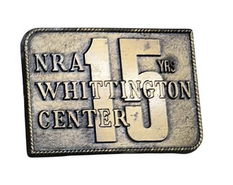 May include: A rectangular bronze-coloured metal plaque with the text "NRA WHITTINGTON CENTER" and "15 YRS" in raised lettering. The plaque has a rope-like border.