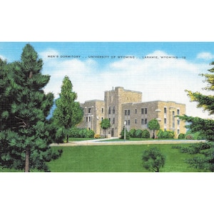May include: Vintage postcard featuring the Men's Dormitory at the University of Wyoming in Laramie. The image shows a large, light-colored stone building with multiple windows, set against a backdrop of a blue sky and green lawn, with trees in the foreground.