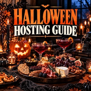 May include: A Halloween Hosting Guide sign above a charcuterie board featuring two red cocktails in stemmed glasses, a carved jack-o'-lantern, a human skull, candles, grapes, figs, cheese, crackers, and cured meats on a dark wooden table.