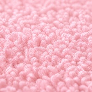 Op de afbeelding: Close-up van een zachte, getextureerde, roze stof. De afbeelding toont een dichte, geluste pool, waardoor een zacht oppervlak ontstaat. De kleur is een licht, pastelroze, wat duidt op een gezellig of delicaat item.