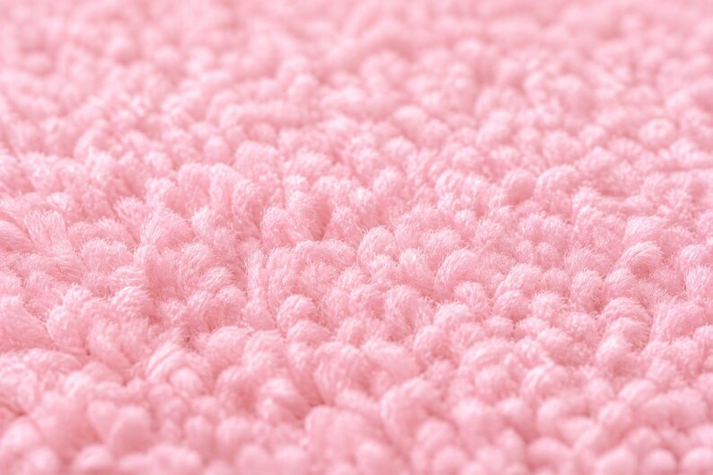 Op de afbeelding: Close-up van een zachte, getextureerde, roze stof. De afbeelding toont een dichte, geluste pool, waardoor een zacht oppervlak ontstaat. De kleur is een licht, pastelroze, wat duidt op een gezellig of delicaat item.