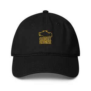 Puede incluir: Gorra de béisbol negra con visera curva. La gorra presenta un gráfico amarillo de un motor y las palabras "CHECK ENGINE" en amarillo, con letras de bloque. La gorra está hecha de un material suave y tiene una corona estructurada.