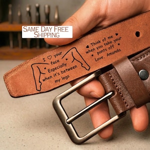 May include: A brown leather belt with a silver buckle. The belt is engraved with the text "I love your face, especially when it's between my legs" and "Think of me when you take your pants off, Love, Amanda."