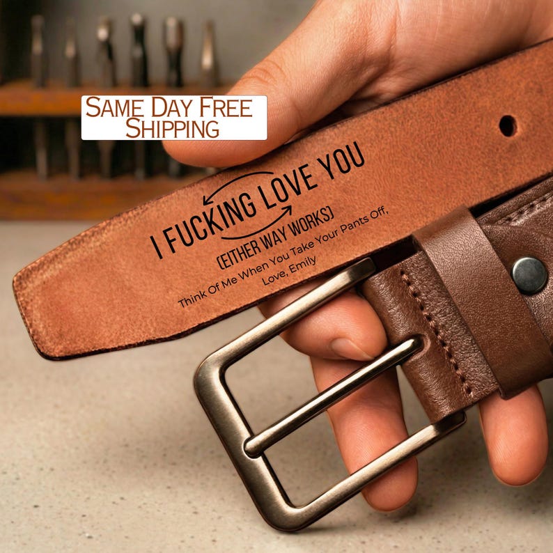 May include: A brown leather belt with a silver buckle. The belt has the text "I FUCKING LOVE YOU" and "(EITHER WAY WORKS)" printed on it. The text "Think Of Me When You Take Your Pants Off, Love, Emily" is also printed on the belt.