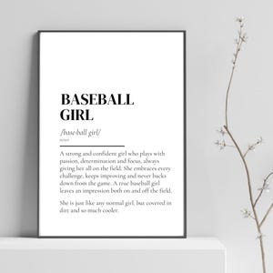 以下が含まれることがあります： 黒字で「BASEBALL GIRL」と書かれた額入りのプリント。その下に、情熱と決意を持ってプレーする自信のある女の子について説明する定義があります。プリントは黒いフレームに入っています。