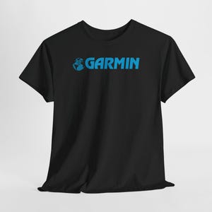 May include: Black t-shirt with the word "GARMIN" in blue, featuring a globe graphic. The shirt is a classic crew neck style, suitable for casual wear. The text is centered on the chest.