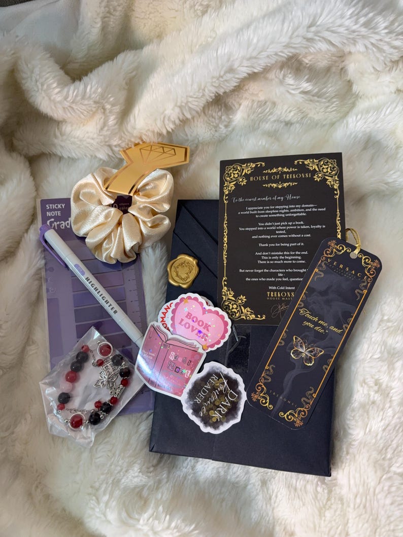 May include: A collection of items including a scrunchie, stickers, a bracelet, a bookmark, and a highlighter. The scrunchie is gold, and the stickers say "Book Lover" and "Dark Romance Reader". The bookmark has a butterfly design.