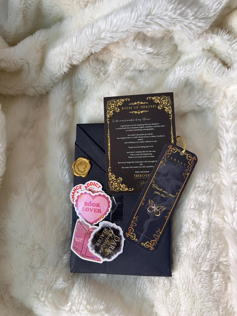 May include: A dark navy gift box with a gold wax seal, stickers, a bookmark, and a card. The stickers read "Romance Addict", "Book Lover", and "Dark Reader". The bookmark has a butterfly design and the text "Touch me, and you die".