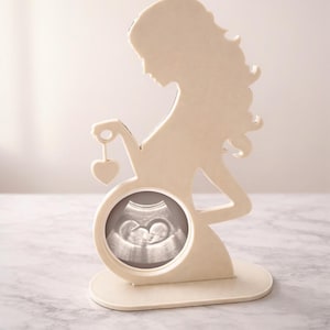 以下が含まれることがあります： クリーム色の妊娠した人のシルエットで、ハート型のチャームを持っています。 シルエットには、胎児のグレースケール超音波画像を表示する円形の開口部があります。 ベースは丸みを帯びた長方形です。