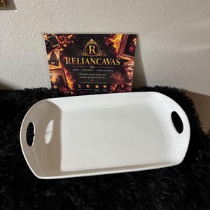 Puede incluir: Una bandeja de servicio rectangular de cerámica blanca con esquinas redondeadas y dos asas ovaladas integradas en los lados. Detrás de la bandeja hay un letrero rectangular con el texto RELIANCAVAS, ARTE HISTORIA COLECCIONES y VINTAGE FIND & CANVAS ART.