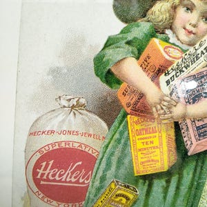 Puede incluir: Anuncio publicitario vintage que presenta a una niña con un vestido verde sosteniendo varias cajas de productos de la marca Hecker, incluyendo avena, trigo sarraceno y harina. También se ve una gran bolsa de harina. La imagen tiene un estilo clásico y antiguo.