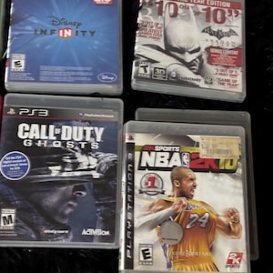 May include: Four PlayStation 3 video games including Disney Infinity 2.0 Edition, Batman Arkham City Game of the Year Edition, Call of Duty Ghosts, and NBA 2K10 featuring Kobe Bryant on the cover, all in their original clear plastic cases.