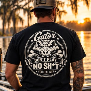 May include: A black t-shirt featuring a white circular graphic on the back. The design displays a stylised alligator head above crossed bones, with the text Gator, DON'T PLAY NO SH*T, and YOU FEEL ME? enclosed within the circular border.