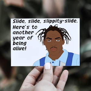 May include: A white card with a cartoon illustration of a man with dreadlocks and the text "Slide, slide, slippity-slide. Here's to another year of being alive!"