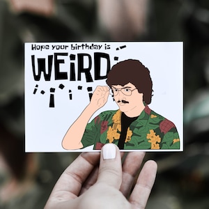 May include: A white card with a cartoon illustration of a man with brown hair and a mustache wearing a green and yellow patterned shirt. The text on the card reads "Hope your birthday is WEIRD!"
