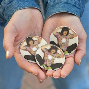 May include: Three round buttons featuring a person in a colorful shirt and black pants. The buttons are held in cupped hands against a denim background. Each button has a white center.
