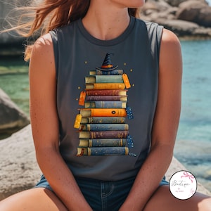 Puede incluir: Camiseta sin mangas gris con un diseño de una pila de libros coloridos coronada por un sombrero de bruja. Los libros tienen etiquetas y estrellas. Un diseño ideal para los amantes de la lectura y los temas de fantasía.