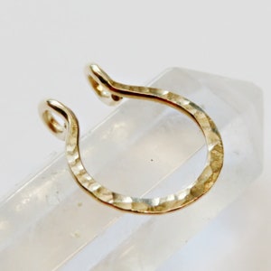 May include: Gold nose ring with a hammered finish. The ring is a simple hoop shape.