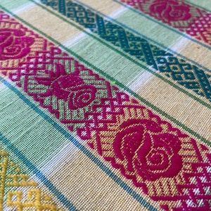 Puede incluir: Primer plano de un textil tejido con un patr&oacute;n repetitivo. La tela presenta rayas alternas amarillas, verdes y turquesas. Atrevidos dise&ntilde;os florales y geom&eacute;tricos fucsia est&aacute;n tejidos en la tela, creando una superficie texturizada.
