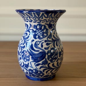 May include: A ceramic vase with a white base and intricate blue floral and bird patterns. The vase has a flared top and a rounded body, showcasing a traditional design. The rim and base are also painted blue.