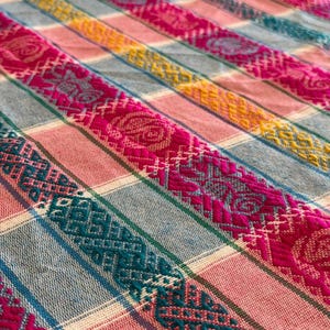 May include: A woven textile featuring a repeating pattern of vertical stripes in shades of magenta, teal, yellow, and light gray. The fabric displays intricate geometric and floral embroidery motifs integrated into the magenta and teal bands.