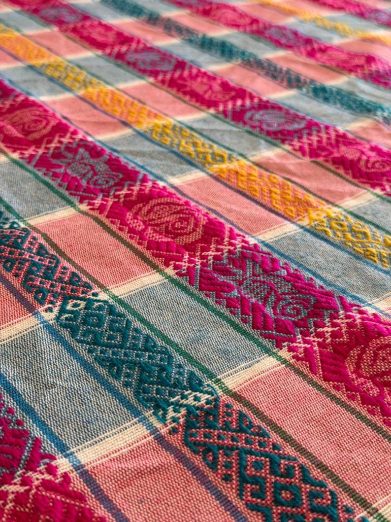 May include: A woven textile featuring a repeating pattern of vertical stripes in shades of magenta, teal, yellow, and light gray. The fabric displays intricate geometric and floral embroidery motifs integrated into the magenta and teal bands.
