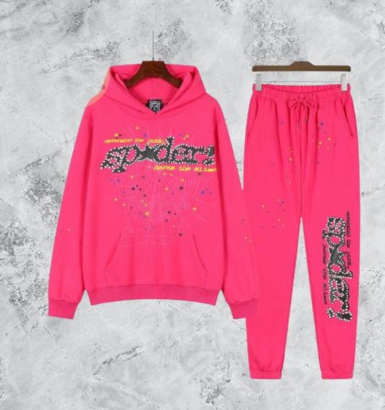 Puede incluir: Conjunto de ch&aacute;ndal rosa brillante que consta de una sudadera con capucha y un pantal&oacute;n de ch&aacute;ndal a juego. La sudadera con capucha presenta un bolsillo delantero y un dise&ntilde;o gr&aacute;fico "Spyder" con una telara&ntilde;a. El pantal&oacute;n de ch&aacute;ndal tiene cintura con cord&oacute;n.