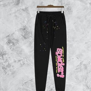 Puede incluir: Pantalones deportivos negros con cintura con cord&oacute;n y bolsillos. Los pantalones presentan un gr&aacute;fico rosa y amarillo que dice "powder!" con el texto "never mind the punk, loves the aliens". Estrellas y puntos coloridos adornan los pantalones.