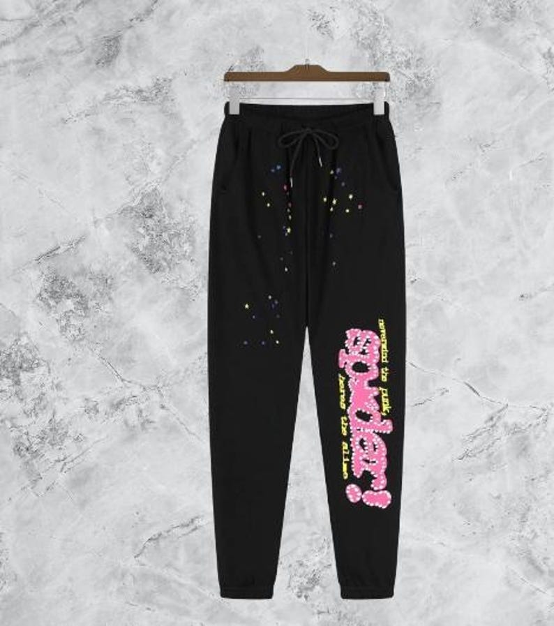 Puede incluir: Pantalones deportivos negros con cintura con cord&oacute;n y bolsillos. Los pantalones presentan un gr&aacute;fico rosa y amarillo que dice "powder!" con el texto "never mind the punk, loves the aliens". Estrellas y puntos coloridos adornan los pantalones.