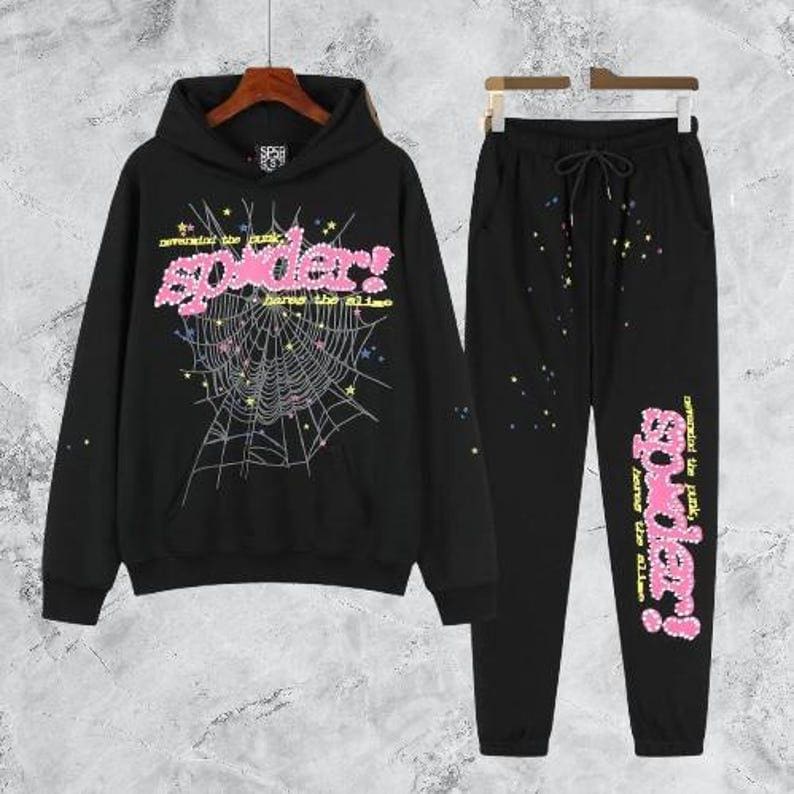 Puede incluir: Conjunto de sudadera con capucha y pantal&oacute;n de ch&aacute;ndal negros. La sudadera con capucha presenta un gr&aacute;fico rosa de "spider!" con un dise&ntilde;o de telara&ntilde;a. El pantal&oacute;n de ch&aacute;ndal tiene un gr&aacute;fico a juego en la pierna y detalles de salpicaduras coloridas.